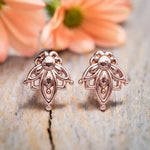 Rose gold earrings on a textured surface with flowers in the background