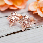 Rose gold earrings on a wooden surface with blurred orange flowers in the background
