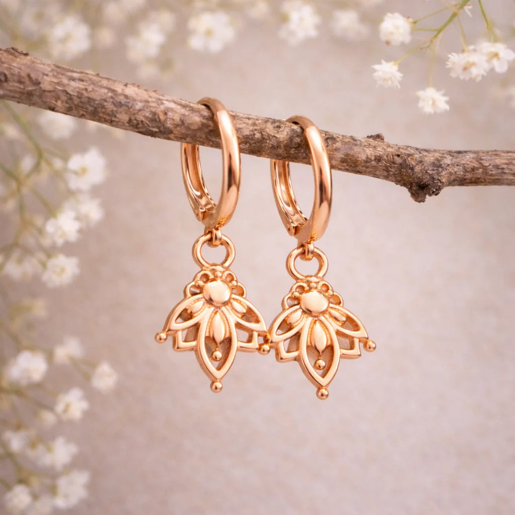Rose gold hoop earrings with floral designs hanging on a branch with white flowers.
