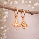 Rose gold hoop earrings with floral designs hanging on a branch with white flowers.