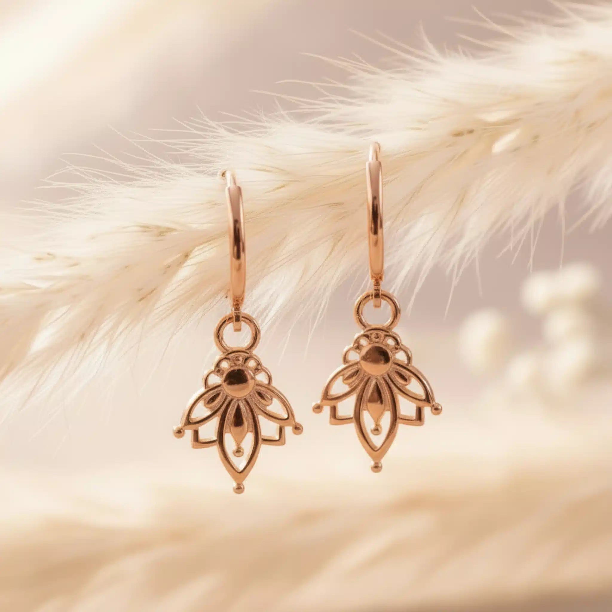 Rose gold hoop earrings with dainty lotus flower charms on a soft beige background
