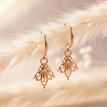 Rose gold hoop earrings with dainty lotus hoop charms on a soft beige background