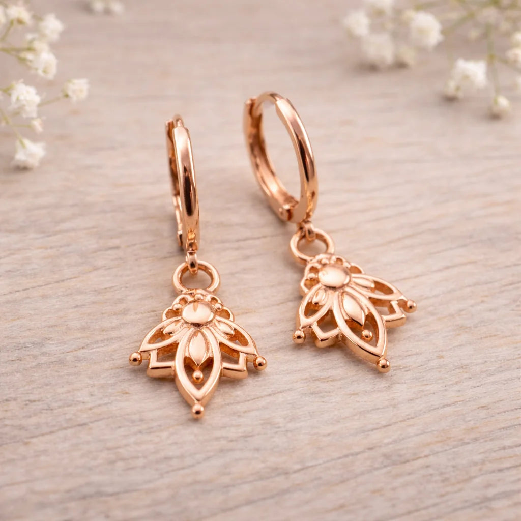 Rose gold hoop earrings with intricate designs on a light wooden surface.