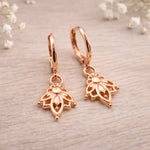 Rose gold hoop earrings with intricate designs on a light wooden surface.