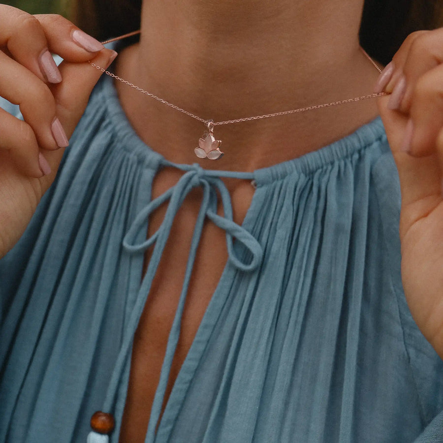 woman wearing a blue dress holding up a rose gold necklace with a lotus flower pendant - rose gold jewellery Australia 