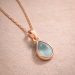 rose gold Necklace with a teardrop-shaped natural aquamarine gemstone pendant on a beige background