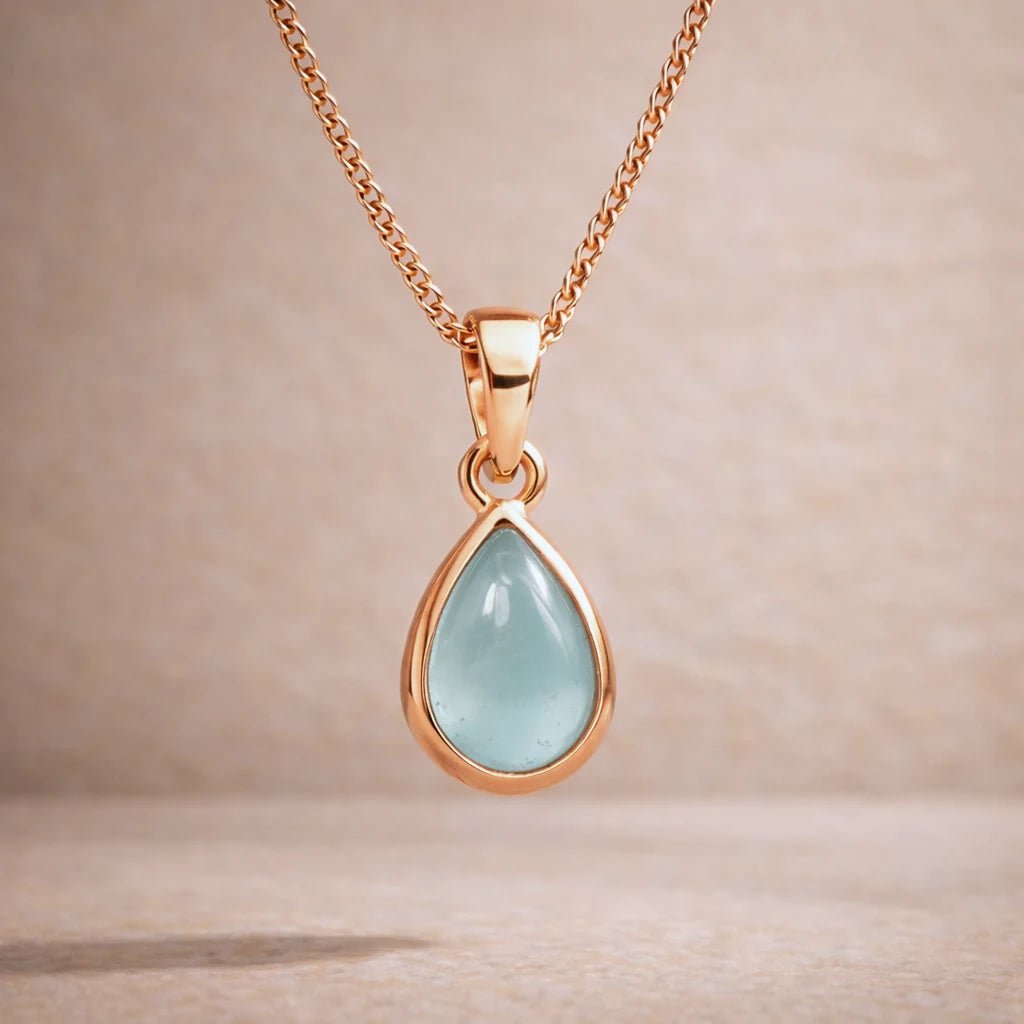 Rose Gold necklace with a teardrop-shaped natural aquamarine gemstone pendant on a beige background