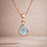 Rose Gold necklace with a teardrop-shaped natural aquamarine gemstone pendant on a beige background