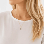 Person wearing a rose gold march birthstone necklace with a aquamarine gemstone pendant, blurred background