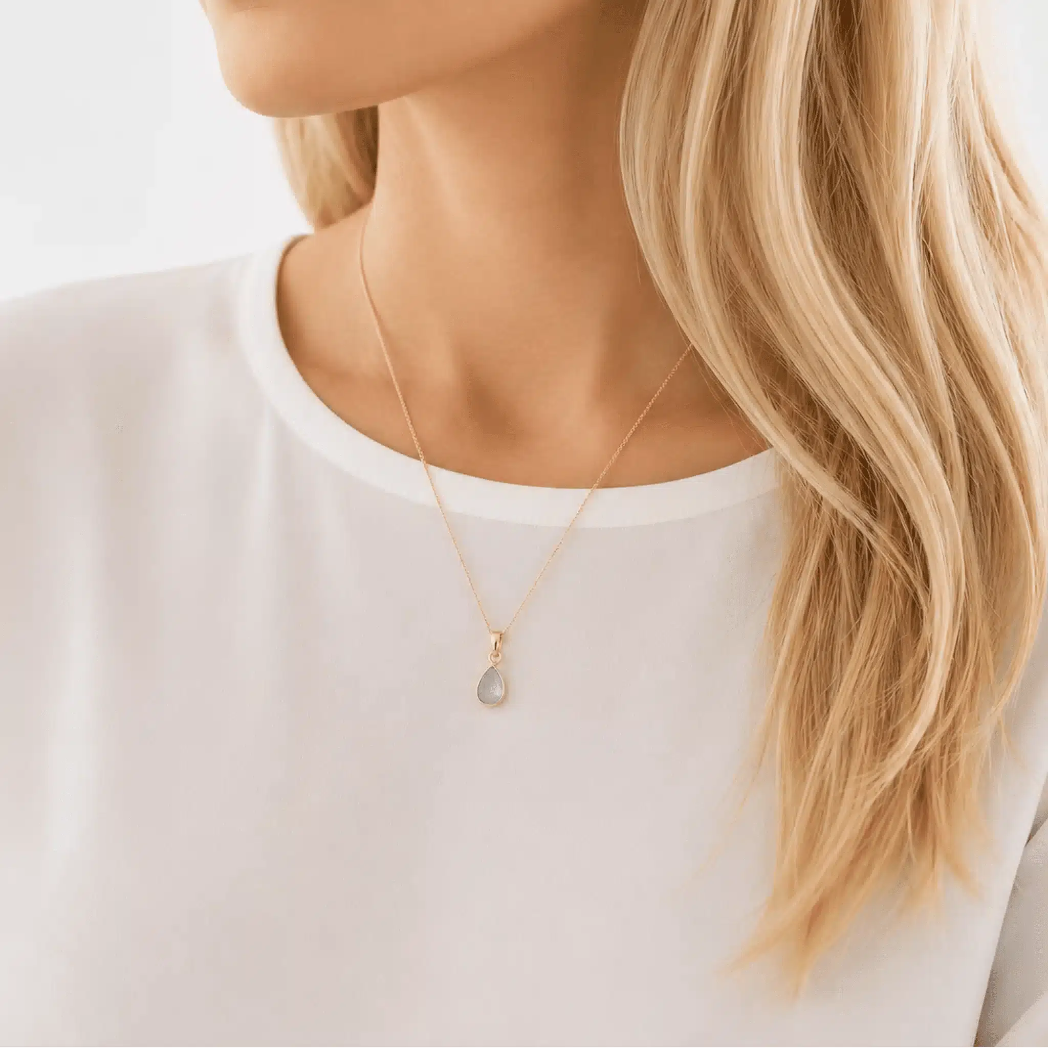 Person wearing a rose gold march birthstone necklace with a aquamarine gemstone pendant, blurred background