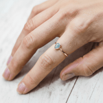 Rose Gold march birthstone ring with a tear drop shaped aquamarine gemstone on a finger against a light background