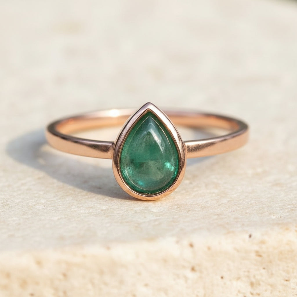 Rose gold ring with a green emerald teardrop gemstone on a wooden surface