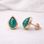 may birthstoneTeardrop-shaped green natural emerald gemstone stud earrings with rose gold settings on a white background