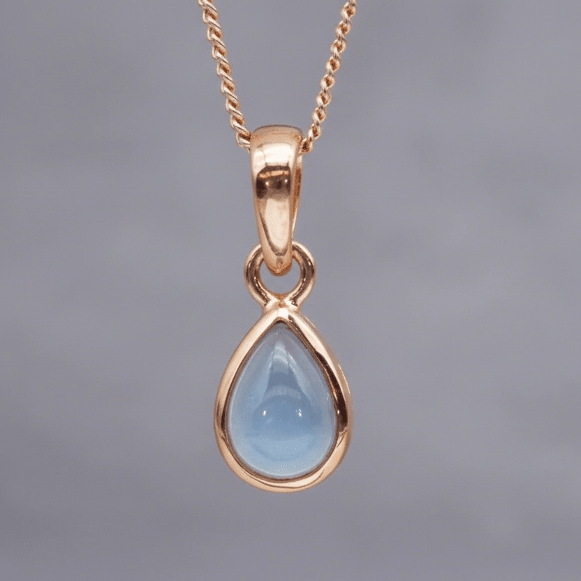 Rose Gold November birthstone necklace with a pear-shaped natural blue topaz gemstone on a grey background