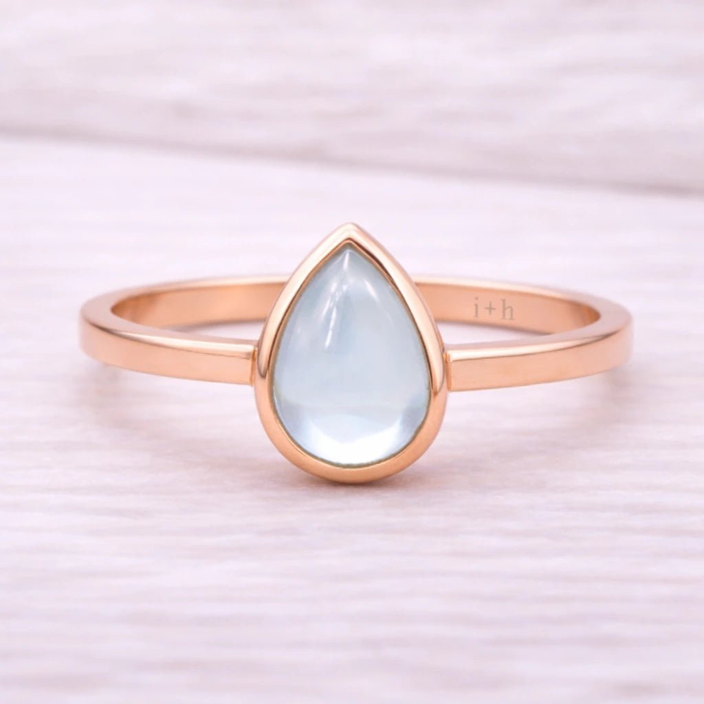Rose gold ring with a teardrop-shaped light blue natural topaz gemstone on a white background