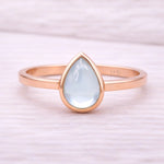 Rose gold ring with a teardrop-shaped light blue natural topaz gemstone on a white background