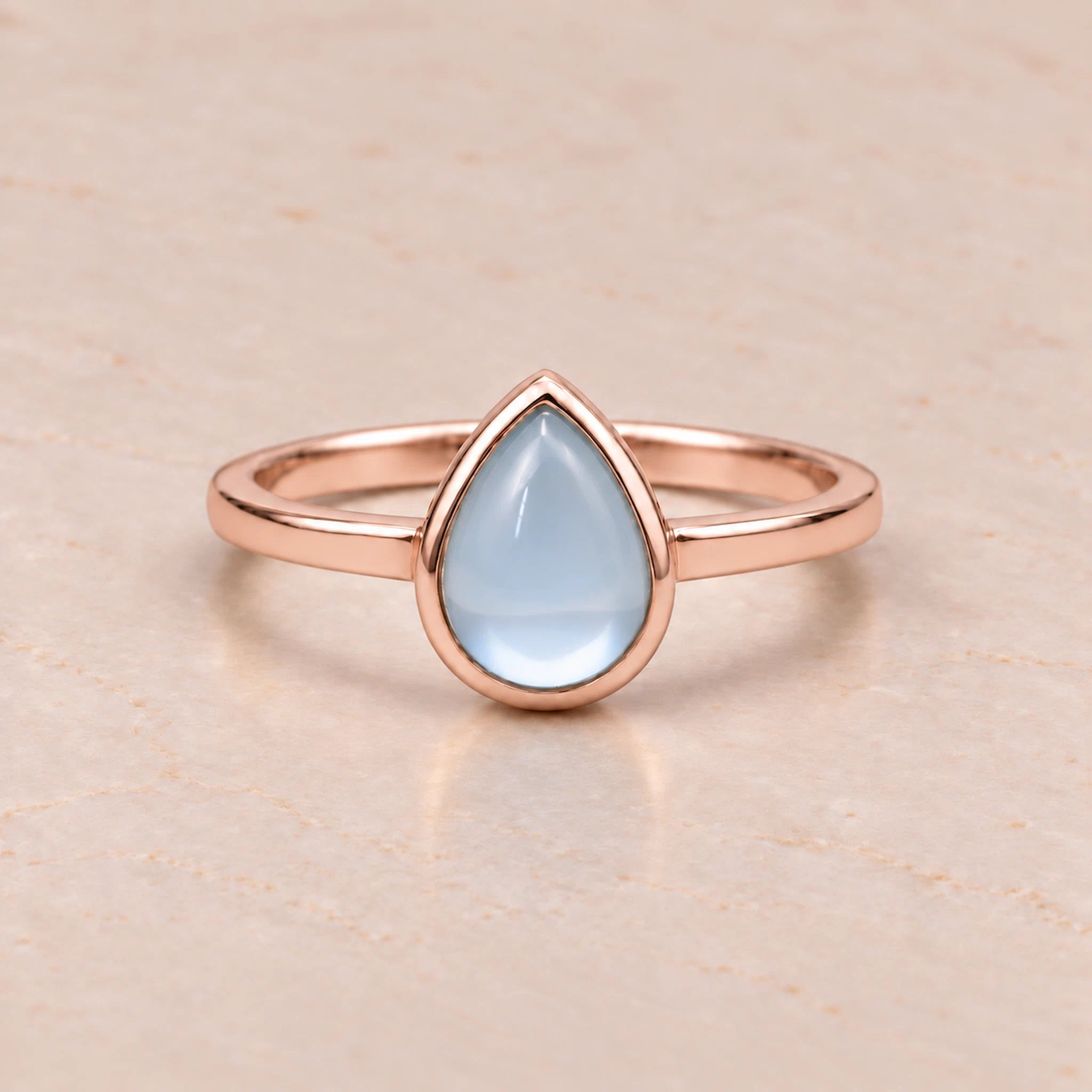 Rose gold November birthstone ring with a teardrop-shaped light blue natural topaz gemstone on a white background