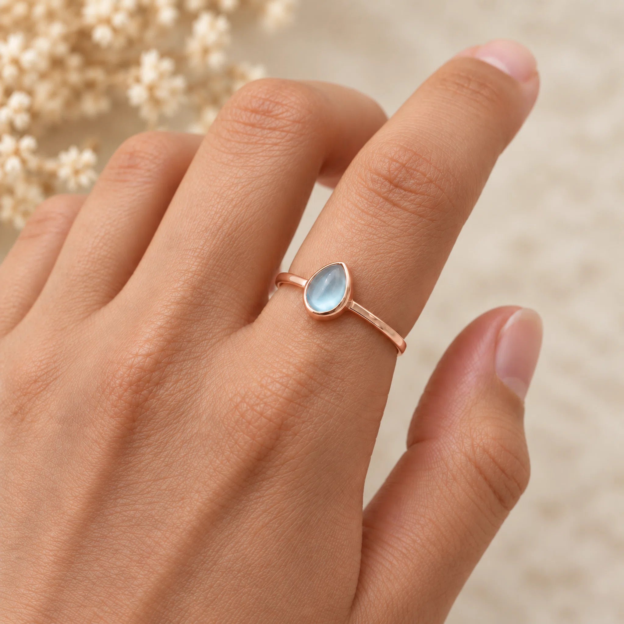 Rose gold November birthstone ring with a teardrop-shaped natural topaz gemstone on a hand against a white background