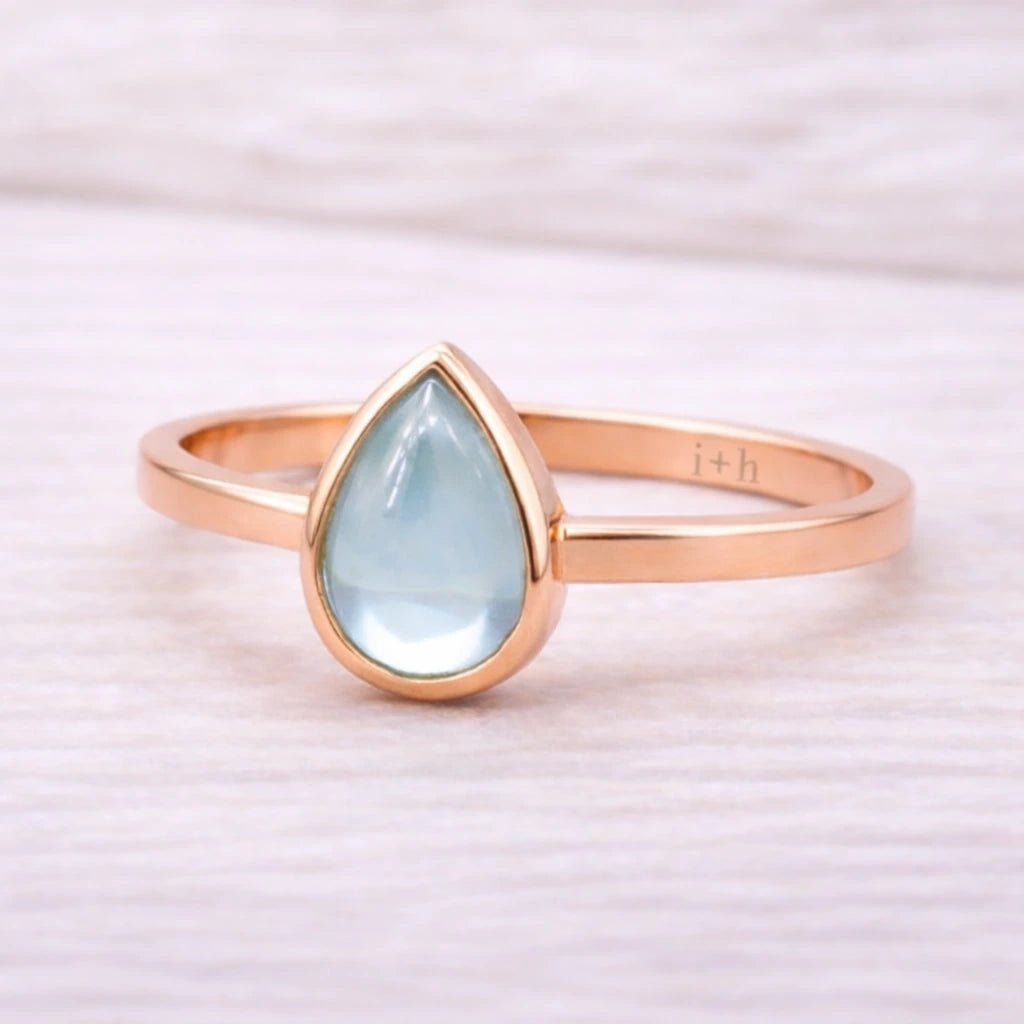 Rose gold ring with a teardrop-shaped light blue natural topaz gemstone on a white background