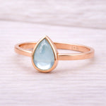 Rose gold ring with a teardrop-shaped light blue natural topaz gemstone on a white background