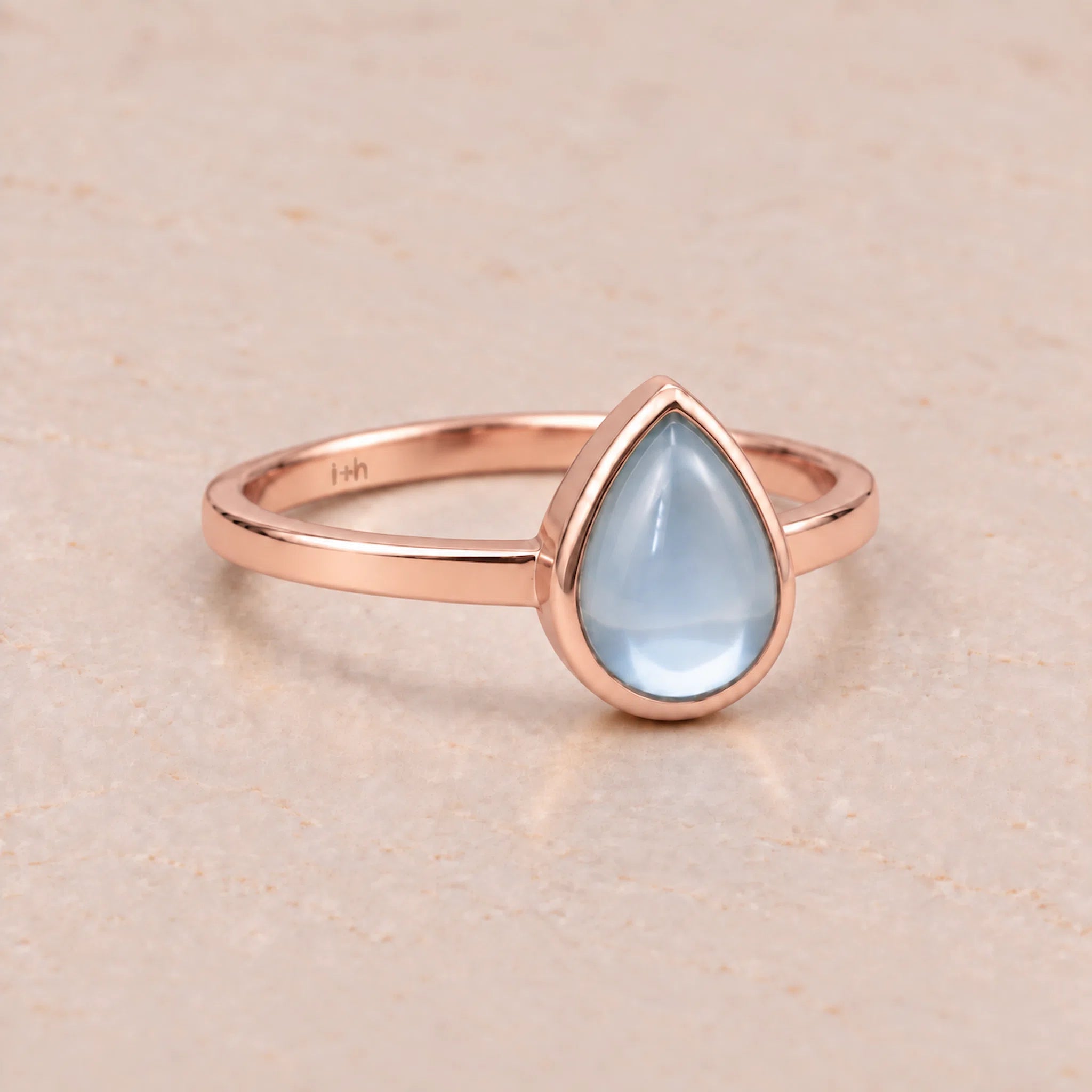 Rose gold November birthstone ring with a teardrop-shaped light blue natural topaz gemstone on a white background