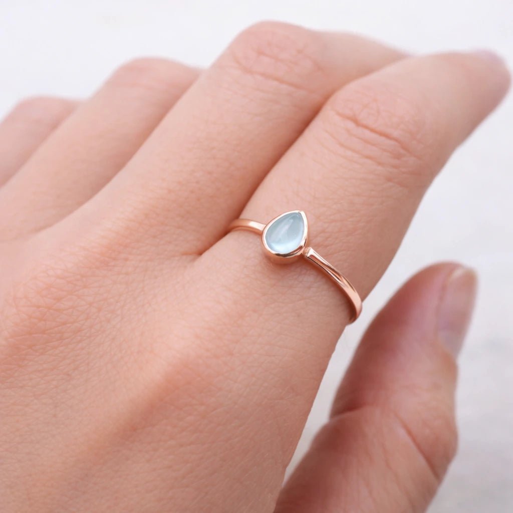 Rose gold ring with a teardrop-shaped natural topaz gemstone on a hand against a white background