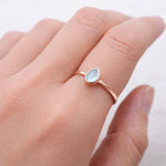 Rose gold ring with a teardrop-shaped natural topaz gemstone on a hand against a white background