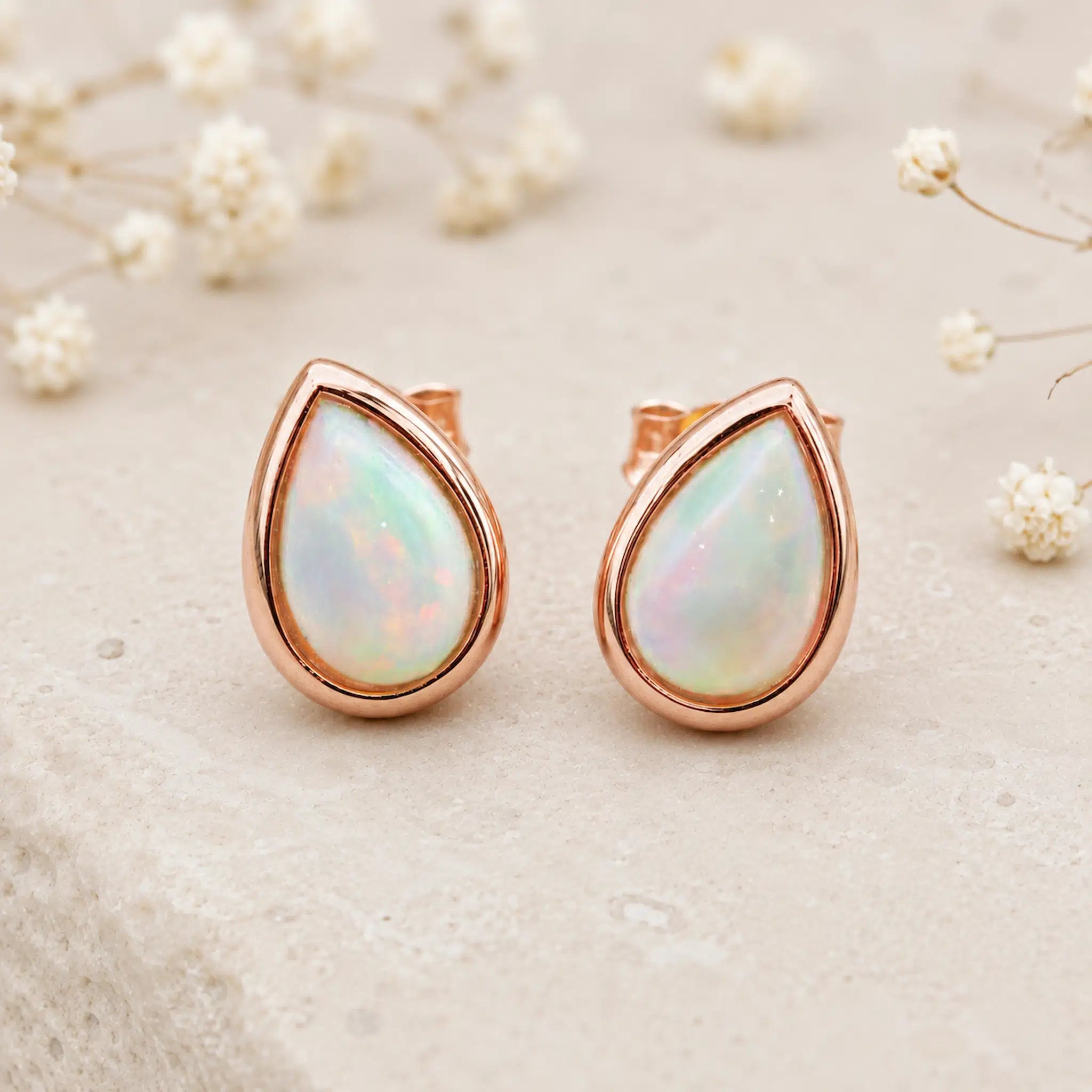 Pair of Rose Gold October Birthstone Earrings in pear-shaped cabochon stud style with natural opal gemstones on a light surface.