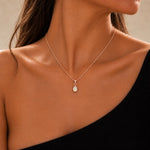 A close-up of a model's neck and upper chest wearing a delicate rose gold chain october birthstone necklace with a teardrop-shaped natural white opal pendant.