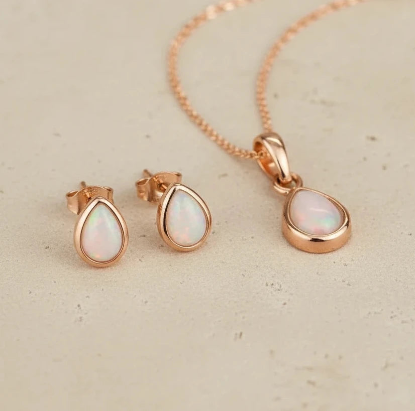 october birthstone opal Jewelry set with rose gold teardrop pendant and earrings on a light stone surface