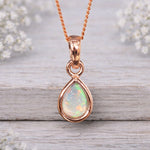 Rose gold October birthstone opal necklace on a wooden surface with flowers