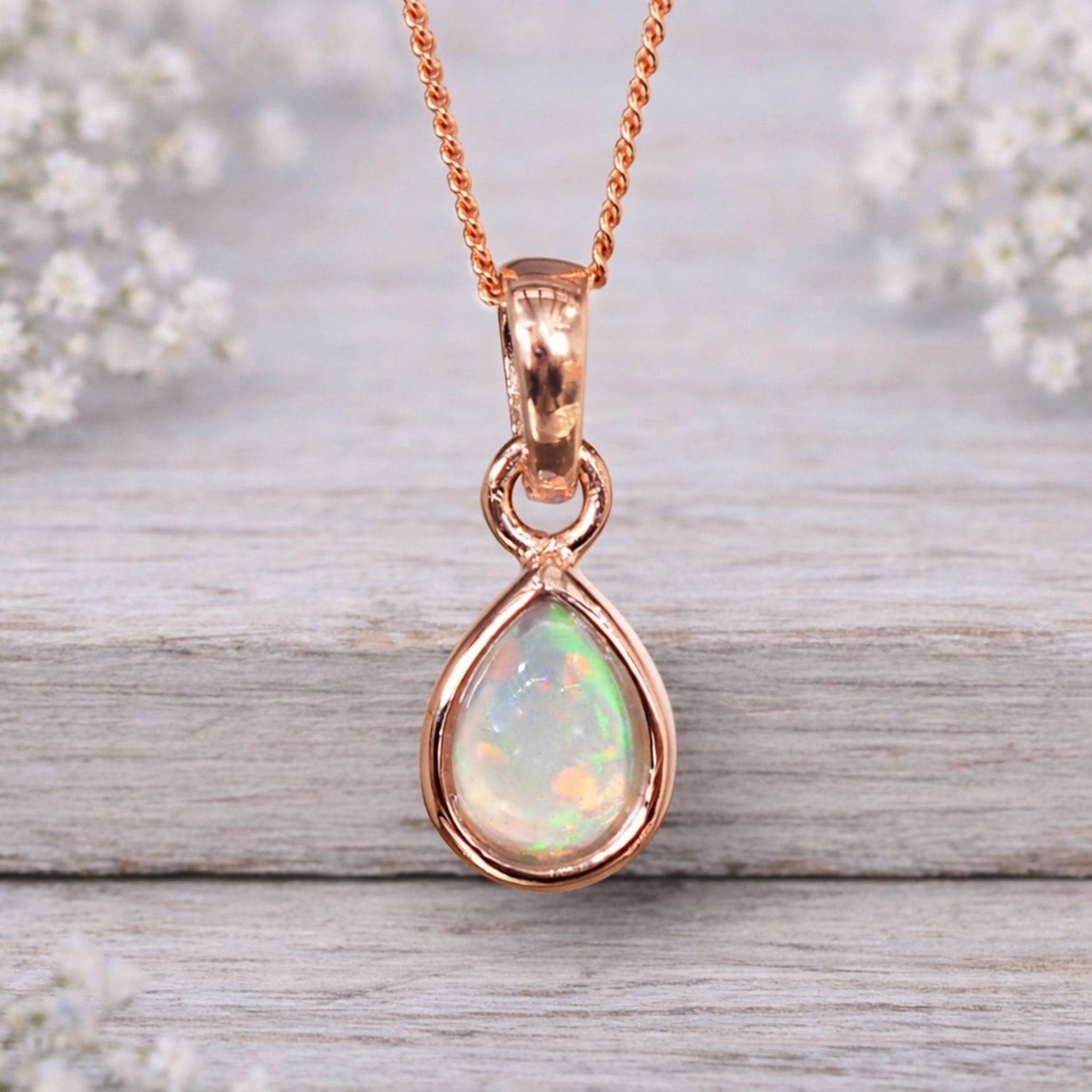 Rose gold October birthstone opal necklace on a wooden surface with flowers