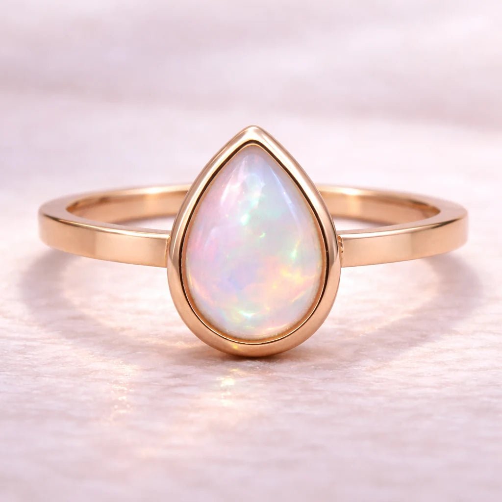 Rose gold ring with a teardrop-shaped opal stone on a soft white background
