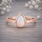 Rose gold ring with a teardrop-shaped opal stone on a wooden surface with white flowers in the background.