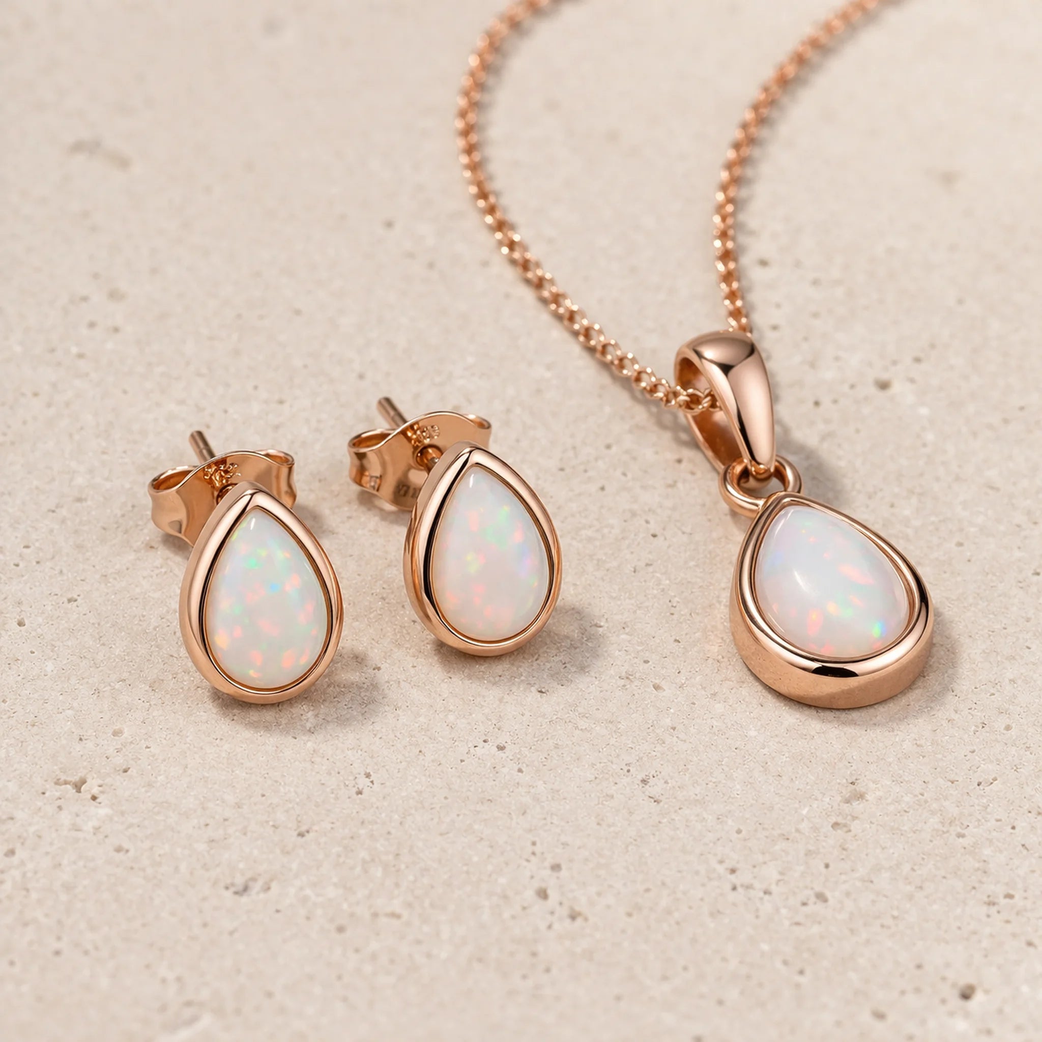 Rose gold jewellery set with opal teardrop earrings and pendant on a beige background