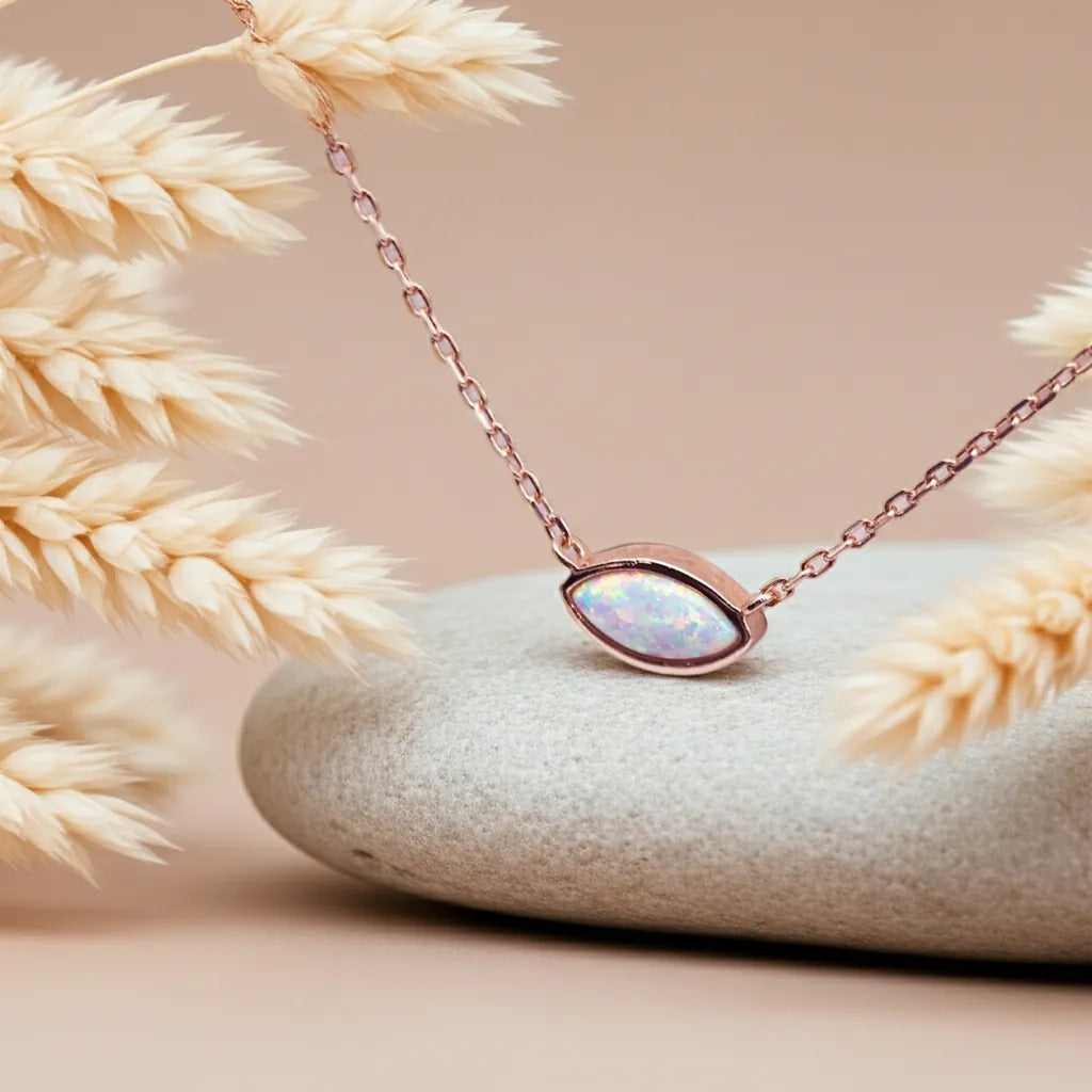 Rose gold necklace with a pendant on a stone surface with dried grasses.