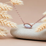 Rose gold necklace with a pendant on a stone surface with dried grasses.