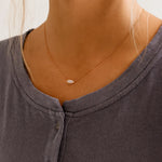 Necklace with a small pendant worn by a person wearing a gray shirt.
