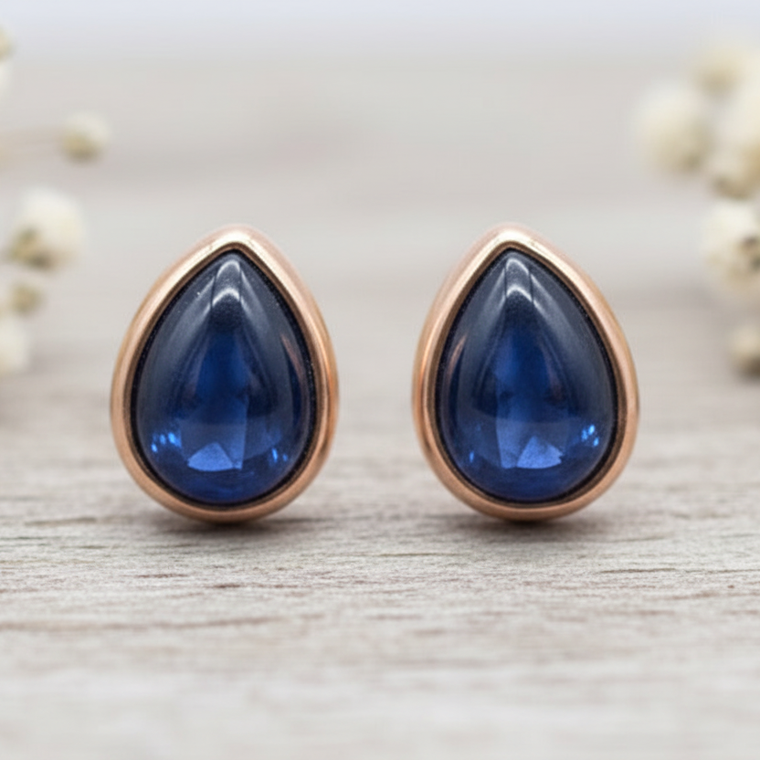 Teardrop-shaped blue sapphire gemstone earrings with rose gold setting on a light wooden surface.