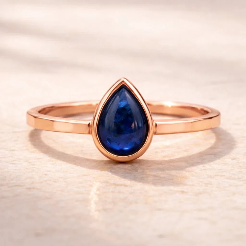 Rose gold ring with a blue teardrop-shaped natural sapphire gemstone on a beige background