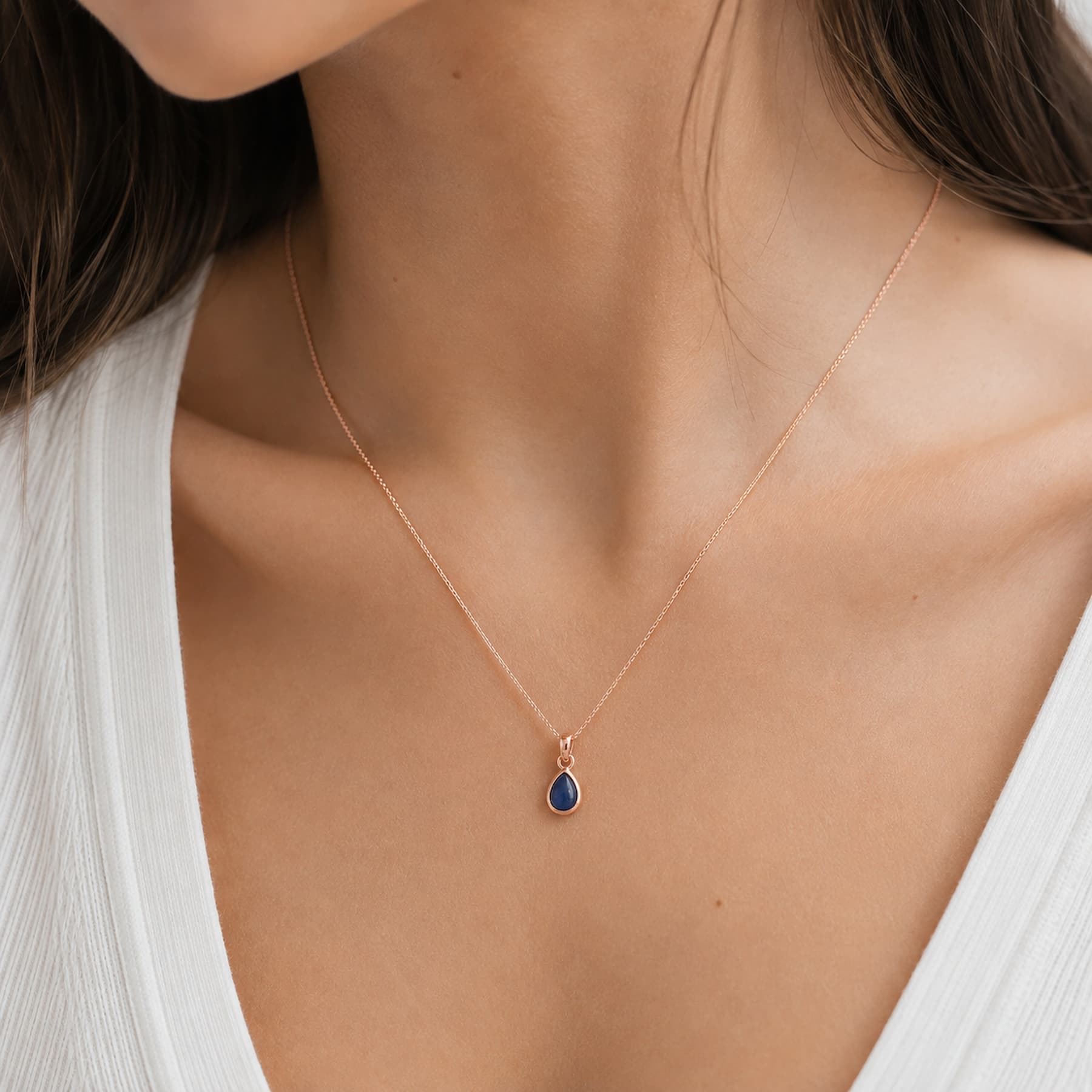 close up of model wearing a dainty rose gold september birthstone natural sapphire teardrop pendant necklace