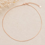 dainty rose gold snake chain necklace on a light stone background