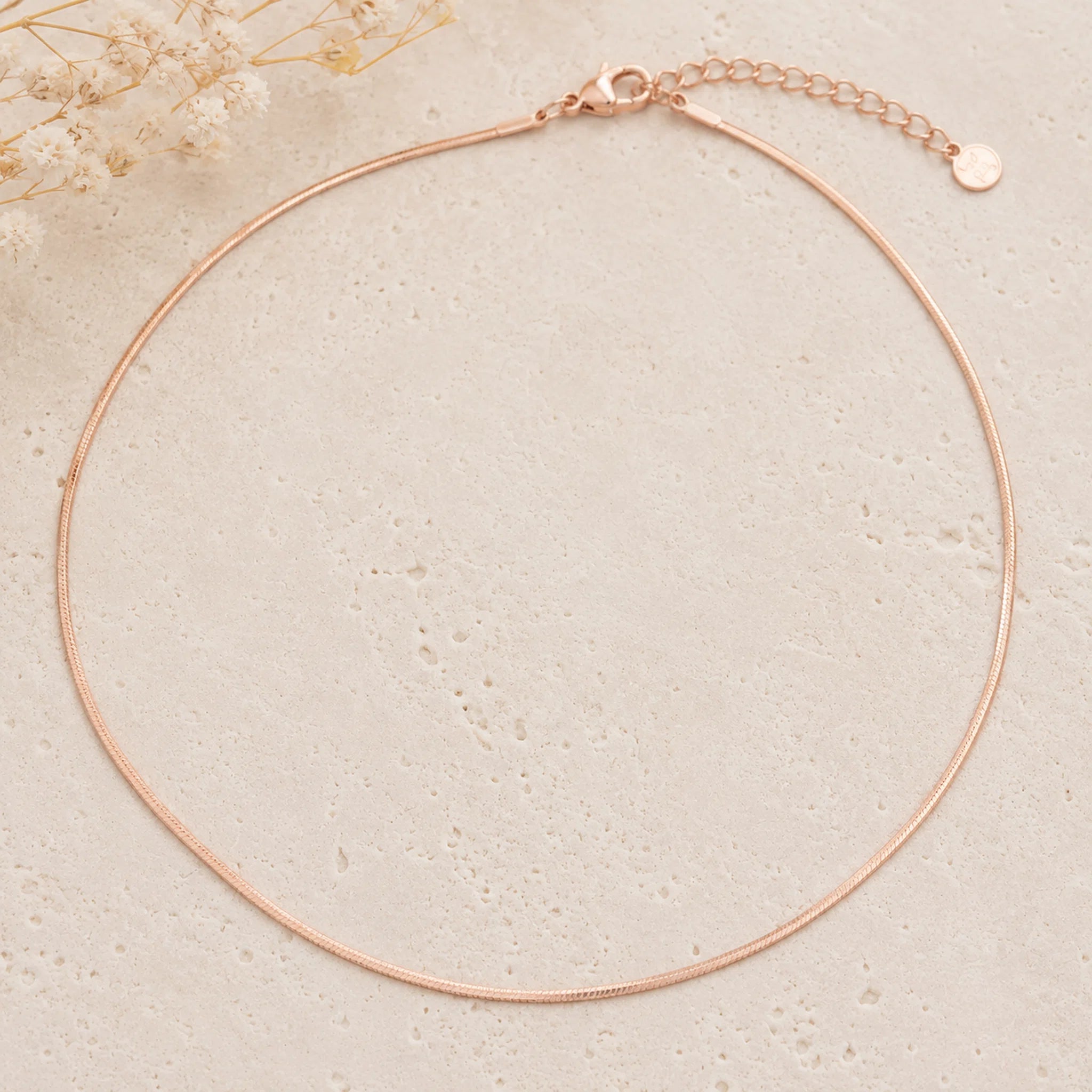 dainty rose gold snake chain necklace on a light stone background