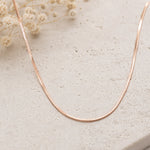 minimalist rose gold snake chain necklace on a stone surface with dried flowers