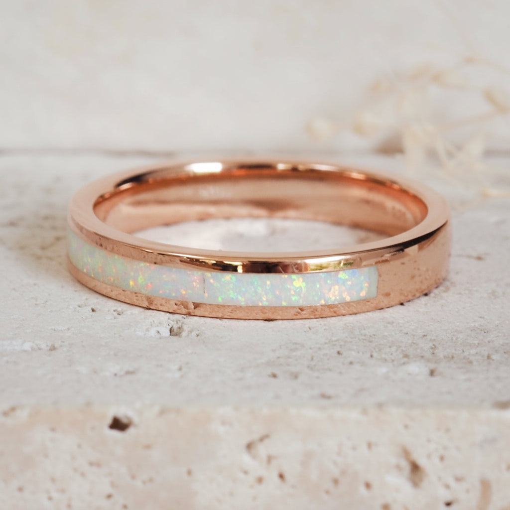 Rose gold ring with white opal inlay on a light stone background