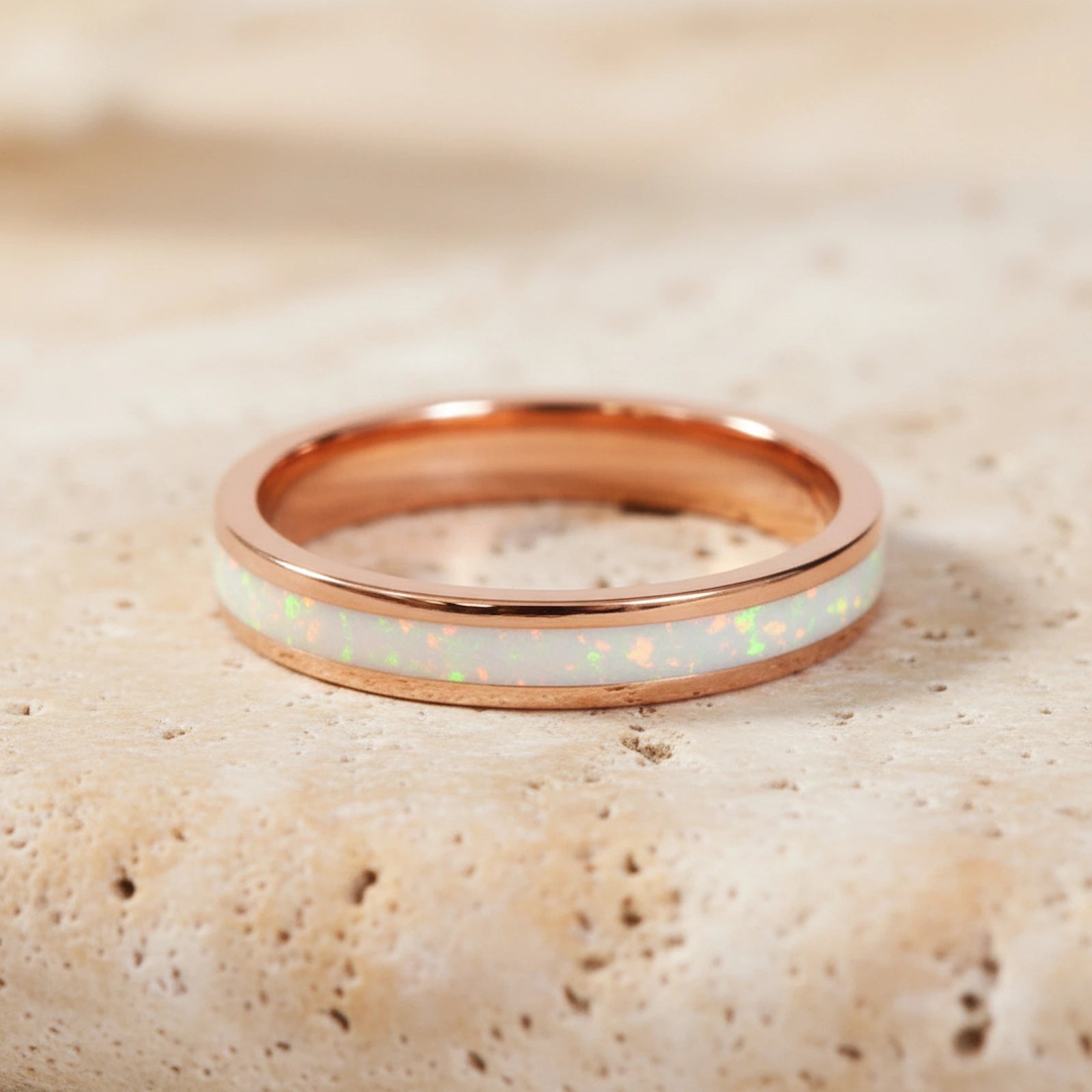 Rose gold ring with white opal inlay on a textured beige surface