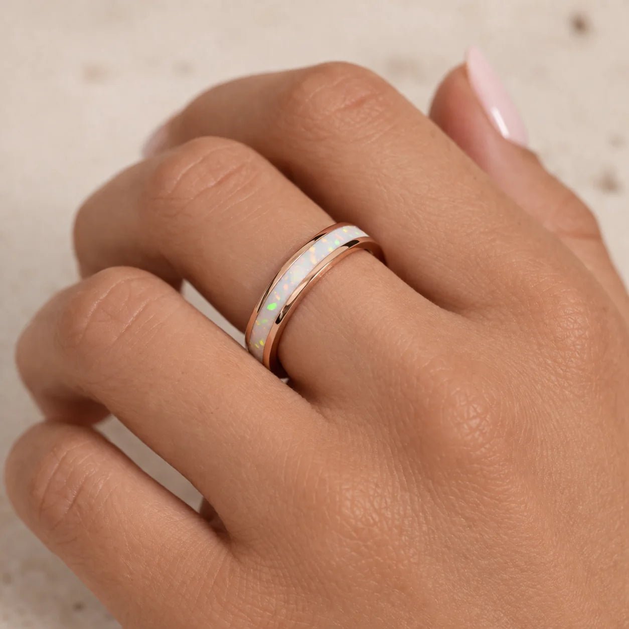 Hand wearing a rose gold band ring with a white opal inlay stone on a neutral background