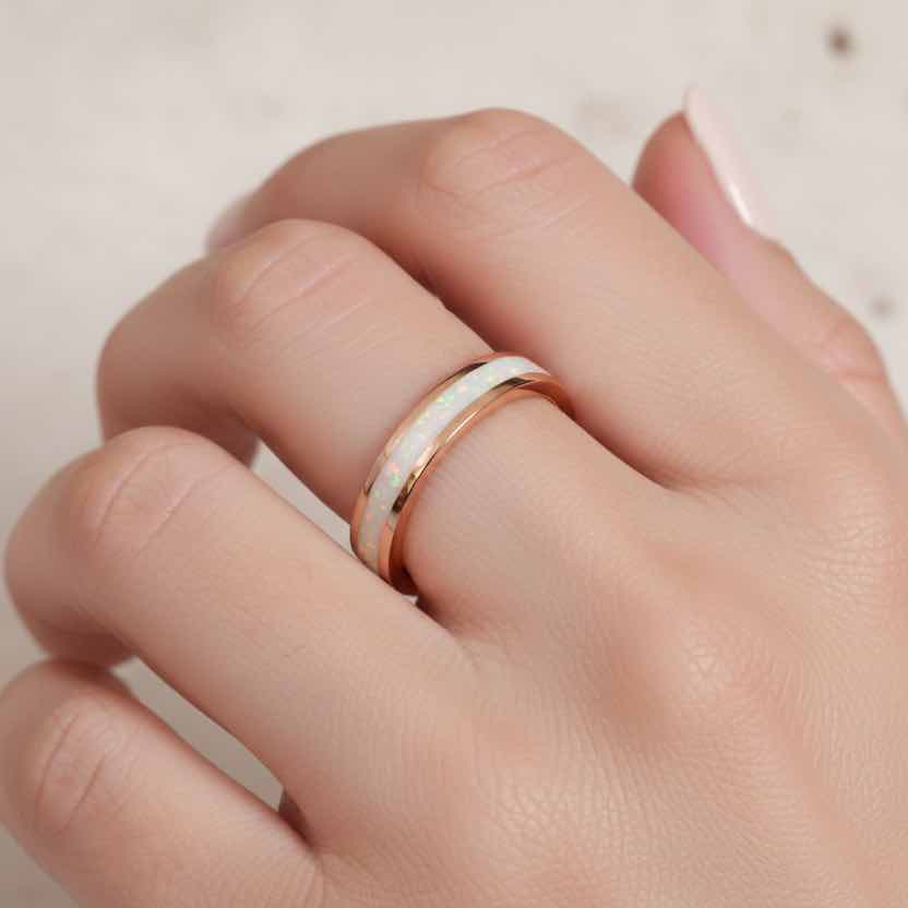 Hand wearing a rose gold ring with a white opal stone on a neutral background