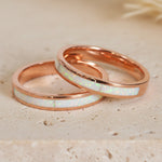 Two rose gold rings with white opal inlay on a beige sand background
