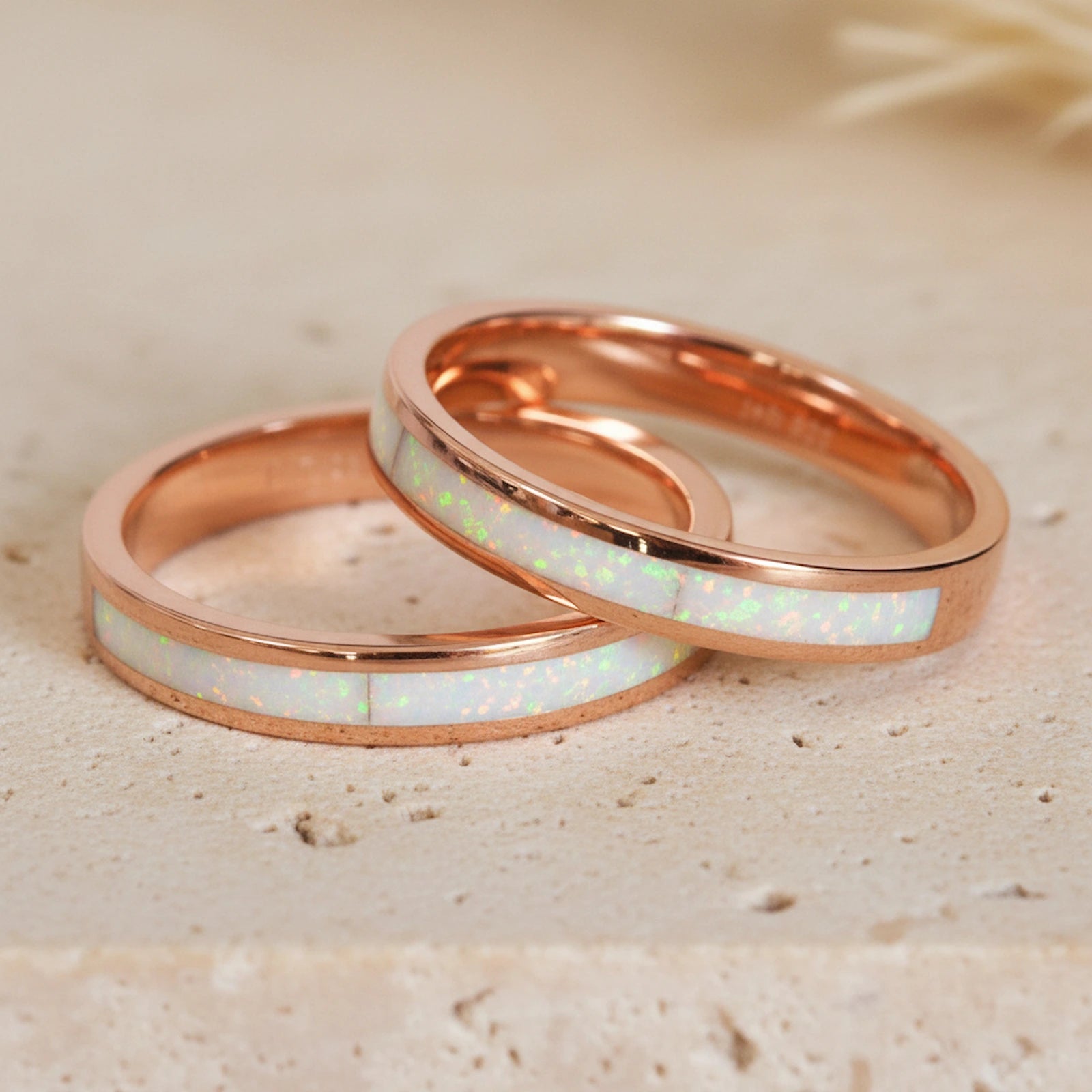 Two rose gold rings with white opal inlay on a beige sand background